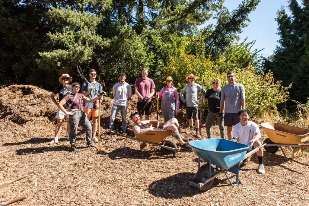 A group of people pose in front of a pile of mulch they're helping to spread.