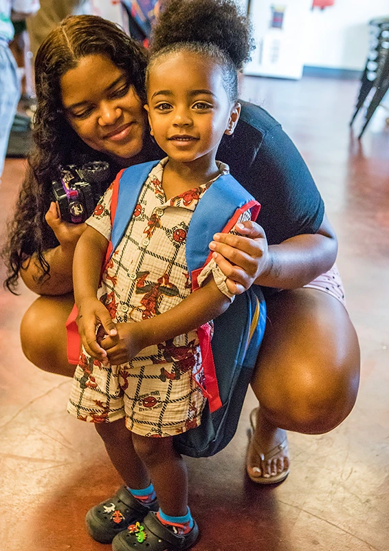 A mom crouches down by her little boy, who's wearing a Spider Man backpack.