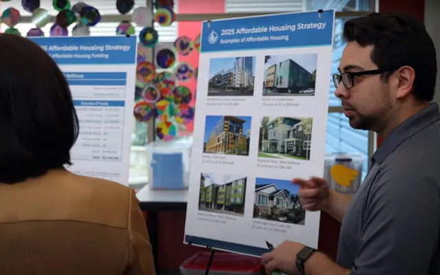 A Bellevue employee explains the city's affordable housing strategy to a woman as he stands by a board showing pictures of housing.