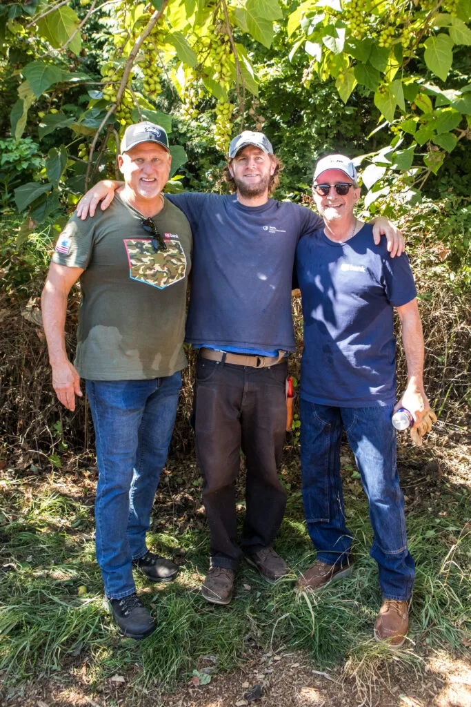 Three men stand outside with arms slung over each other's shoulders.