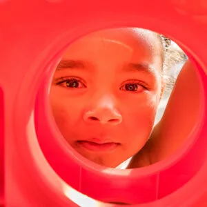 A little boy peeks through a circle in a red plastic game.