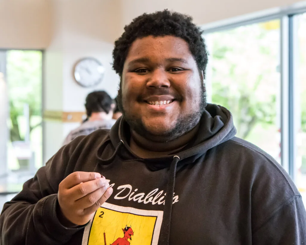 A cooking class student in a black hoodie smiles at the camera.