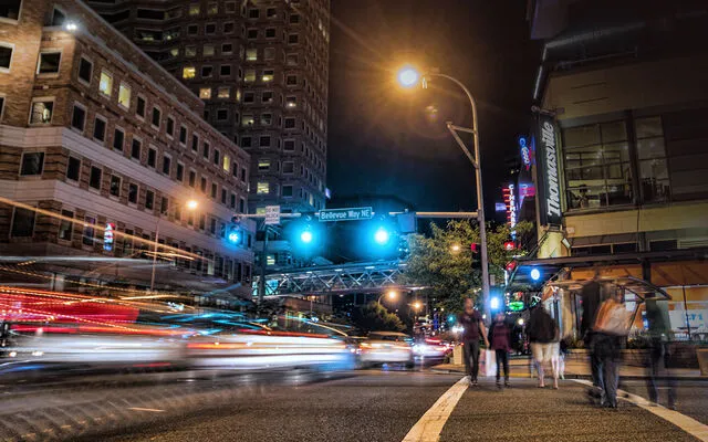 Cars and pedestrians cross an intersection in downtown Bellevue at night.