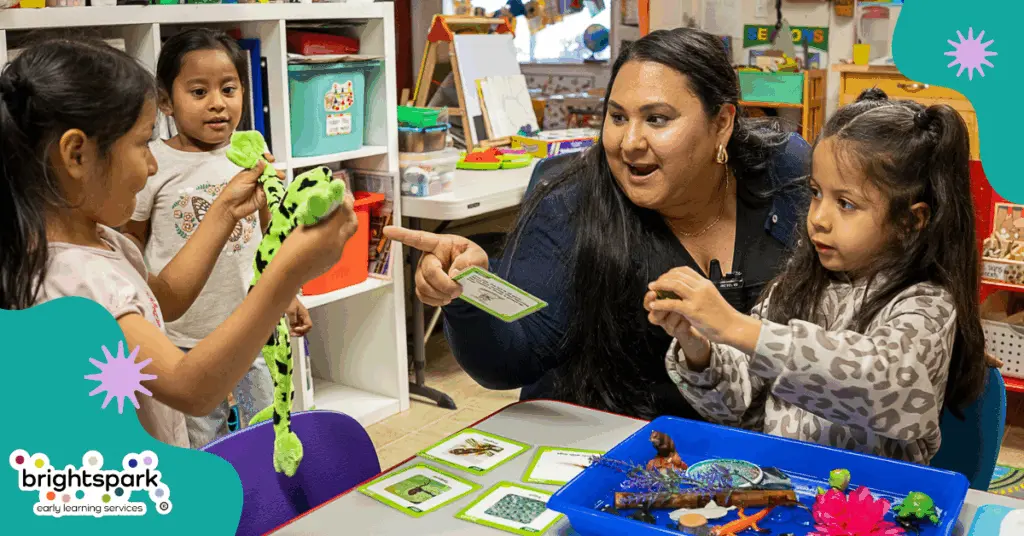 Provider with child on their lap points to another child holding a green frog while another child watches