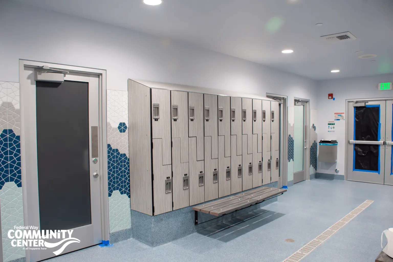 FWCC locker room cabanas with a row of light wood lockers, a bench underneath, and cabana doors on both sides.