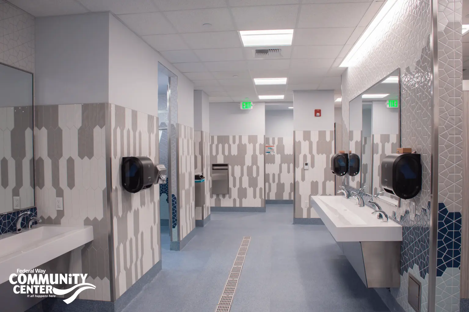 FWCC locker room restroom with patterned tile walls, multiple sinks, mirrors, and paper towel dispensers.