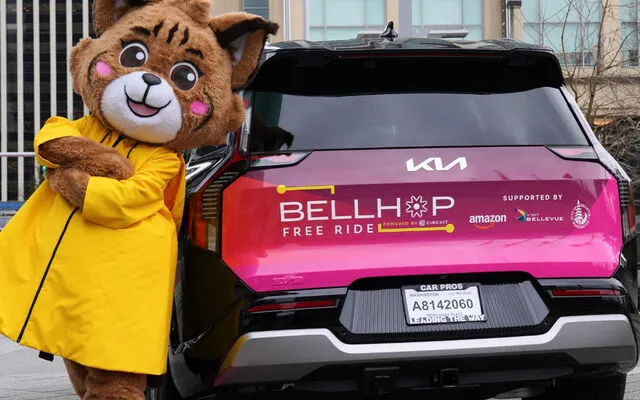 Belle the Bobcat, Visit Bellevue's mascot, leans against a BellHop shuttle.