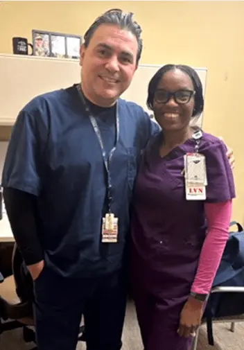 Two health care professionals smiling in an office. One wears navy scrubs, the other purple with an LVN badge.