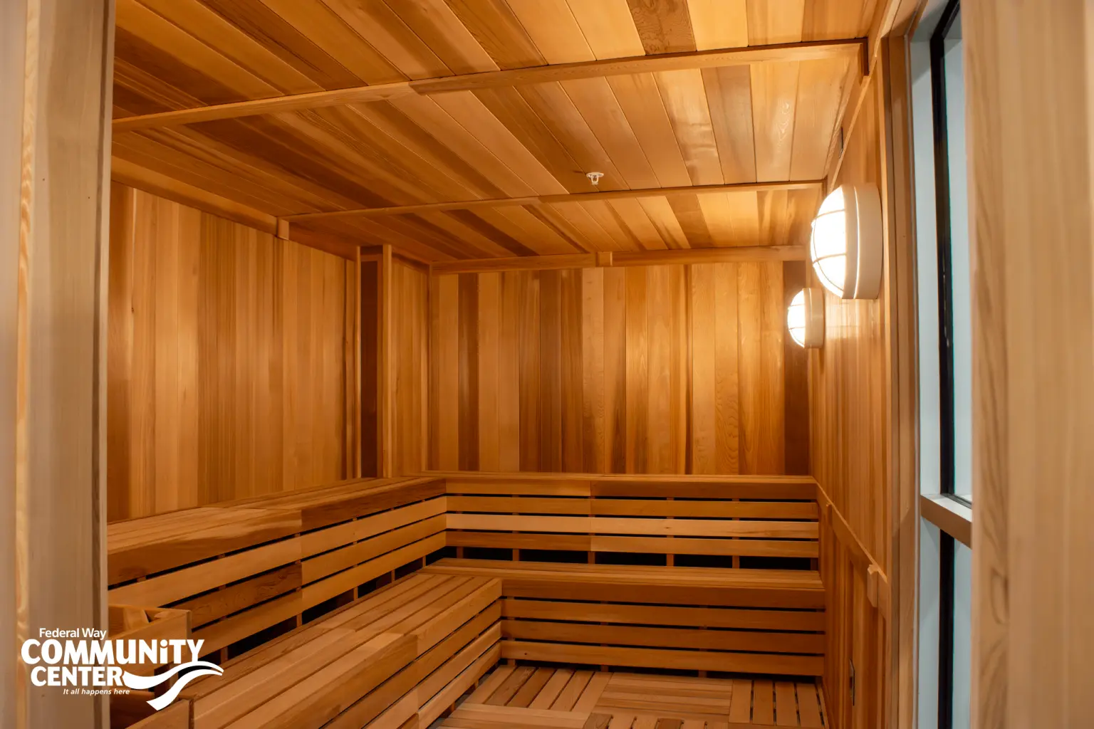 Wood-paneled sauna interior with bench seating and wall-mounted lights at the Federal Way Community Center.