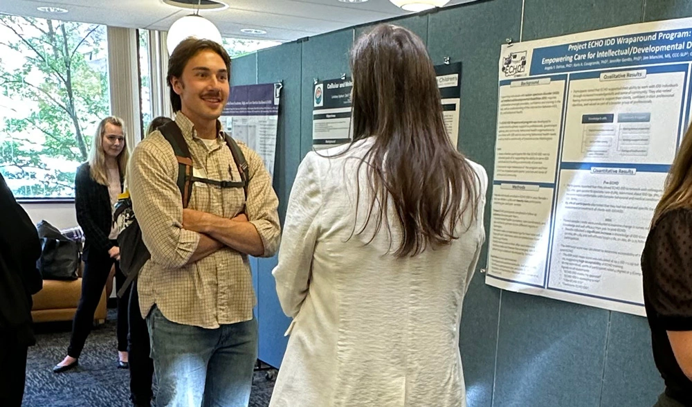 Photo: Poster presentation with a presenter answering questions at Research Day.