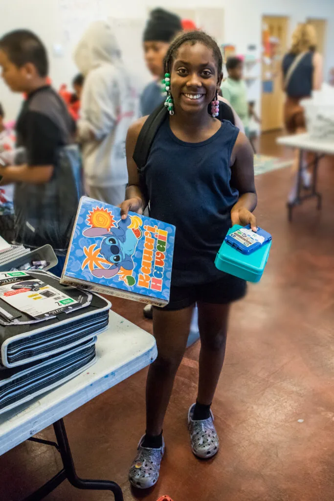 A girl with beaded braids shows off several new school supplies.