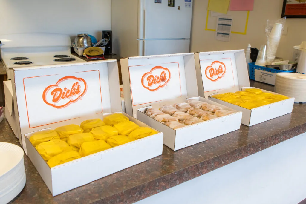 Three boxes labeled "Dick's" and filled with hamburgers sit on a countertop.