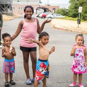 Three little kids and one tween, wearing summer clothes and bathing suits, eat ice cream cones.