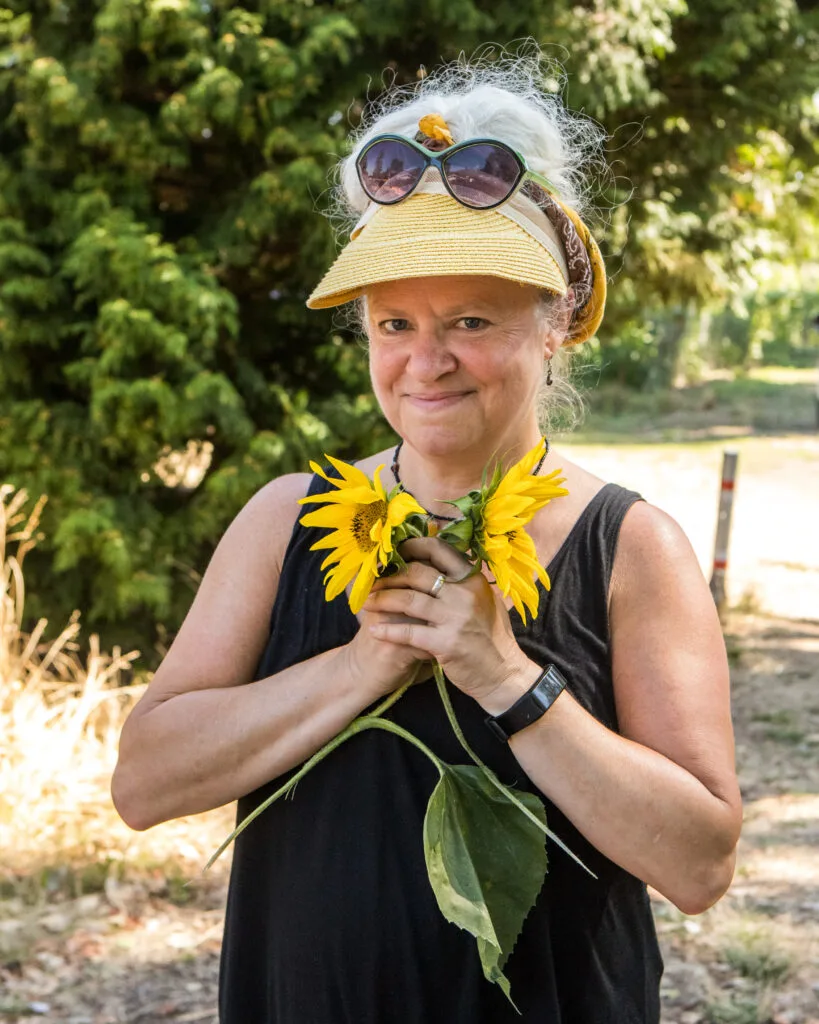 A woman in a yellow visor clutches a handful of sunflowers.
