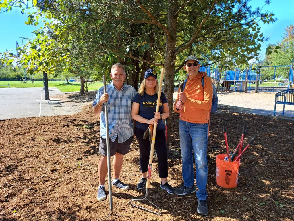 Three people pose under a tree surrounded by a fresh layer of mulch.